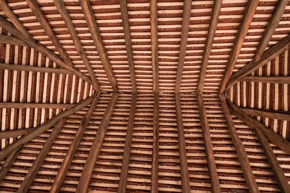 A network of wooden roof batten rafters in an overhead view, showing the traditional hand cleft finish.