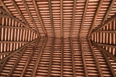 A network of wooden roof batten rafters in an overhead view, showing the traditional hand cleft finish.