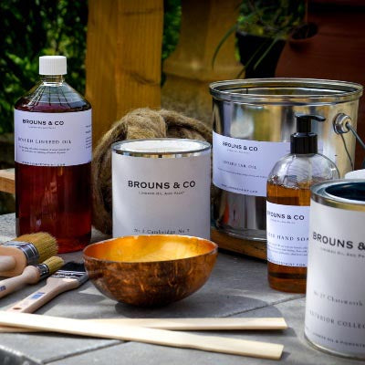 Brooms & Co products including bottles, a can, a bowl, and brushes on a stone surface with a wooden background.