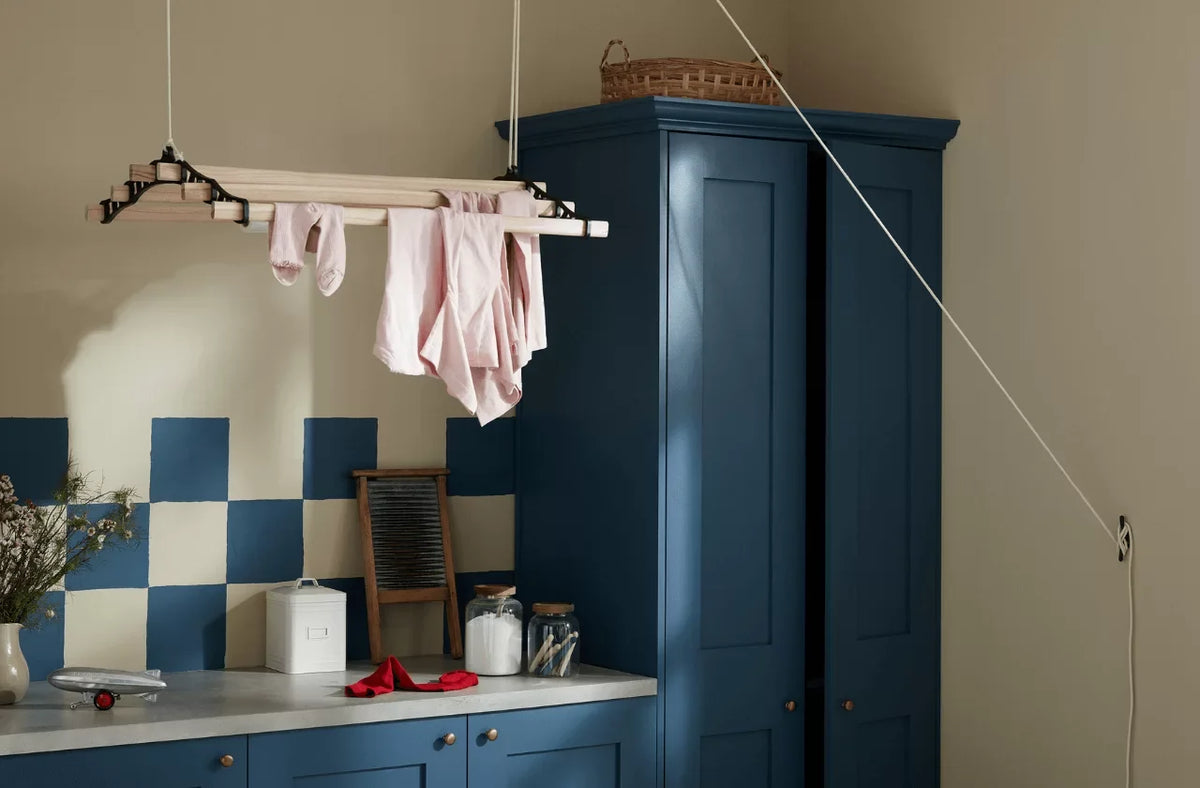 Laundry room with hanging clothes, blue cabinets, and checkered wall.