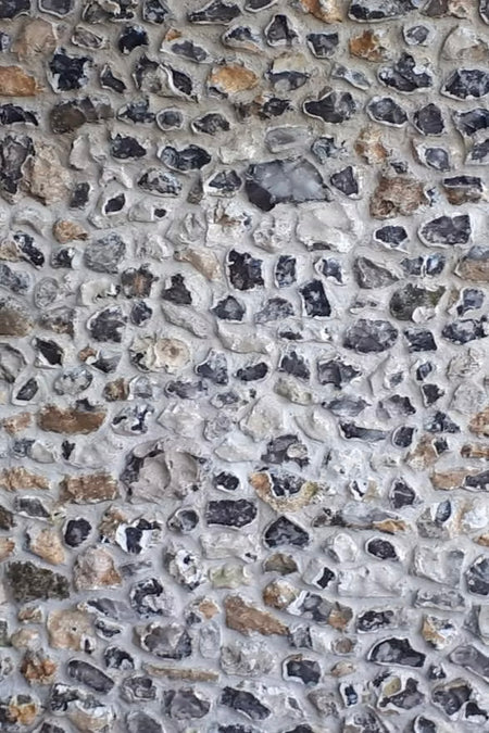 A close-up image of a field flint semi-knapped stone, showing varying shades of brown, grey, black, blue, and white, with a mix of natural and knapped faces.