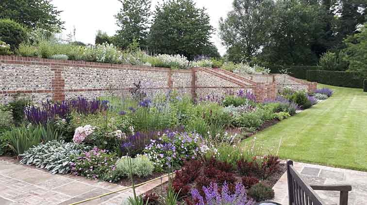 flint and brick garden wall with full beds of flowers and lawn in the foreground