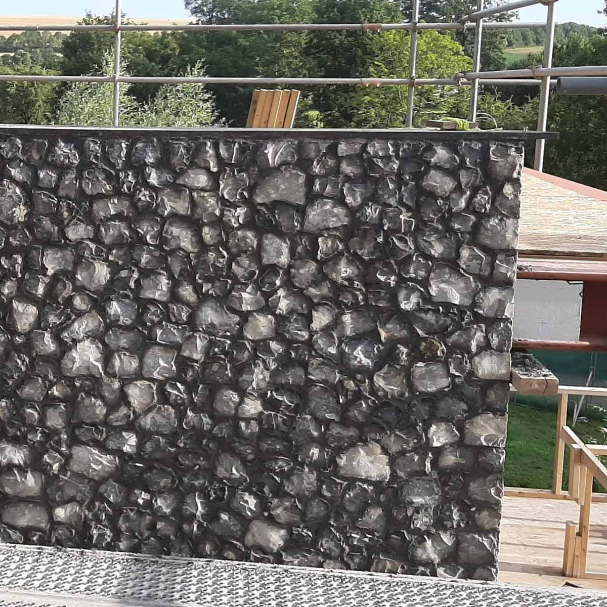 picture of a grey flint wall with clean sharp corner detail. on a building site with scaffolding 